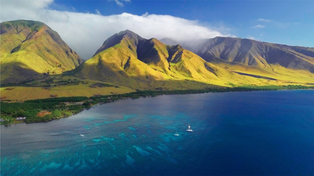 aerial view of the west coast of maui with visible coral reef and green mountain on the background