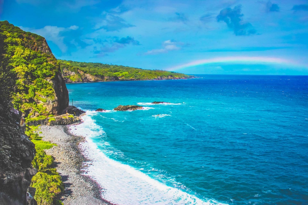 waves crashing a maui beach with a rainbow in the distance on the road to hana maui