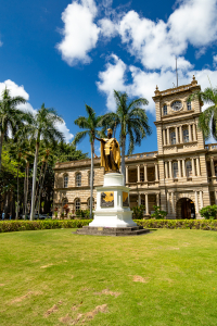King Kamehameha I statue in front of Aliiolani Hale in Honolulu, Oahu Hawaii with palm trees and American flag