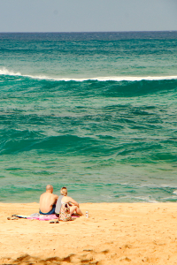 Couple sitting on sandy North Shore beach in Oahu Hawaii watching turquoise waves
