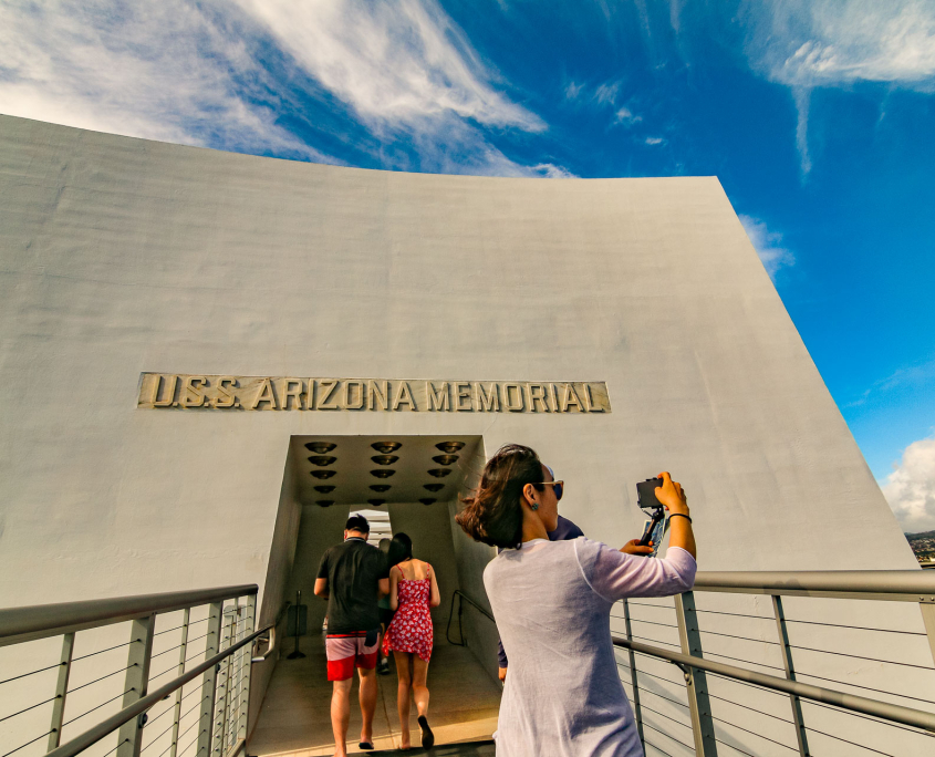 Visitors entering the USS Arizona Memorial at Pearl Harbor, Oʻahu, with a woman taking a photo at the entrance