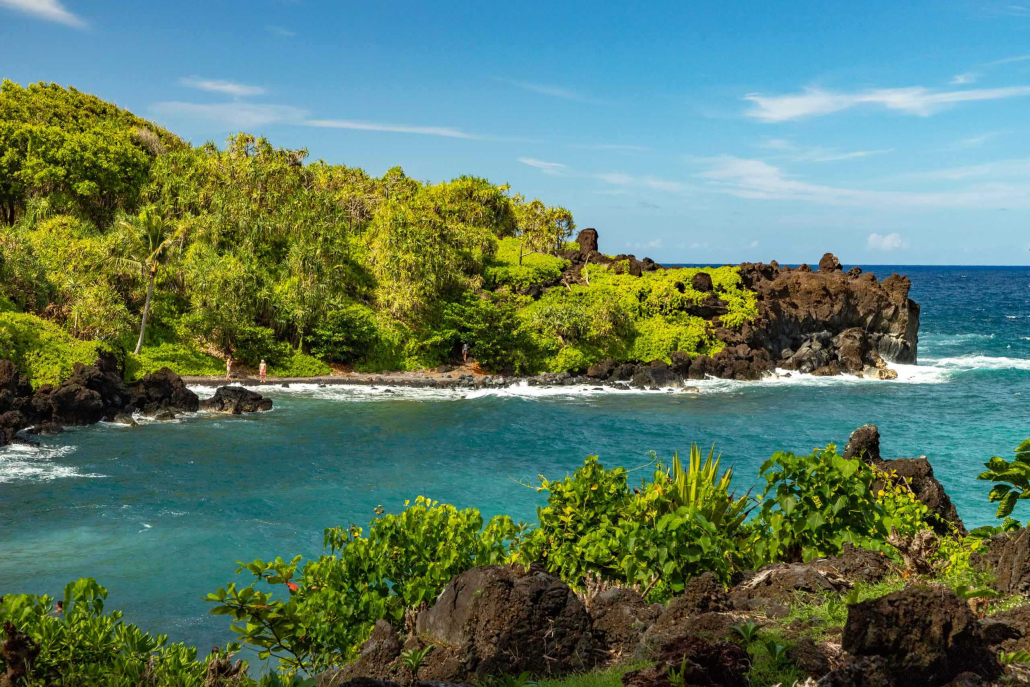 Waianapanapa Black Sand Beach, Road to Hana, Maui Scenic view of Waianapanapa Black Sand Beach along the Road to Hana in Maui, with lush greenery, lava rock formations, and turquoise ocean waves.